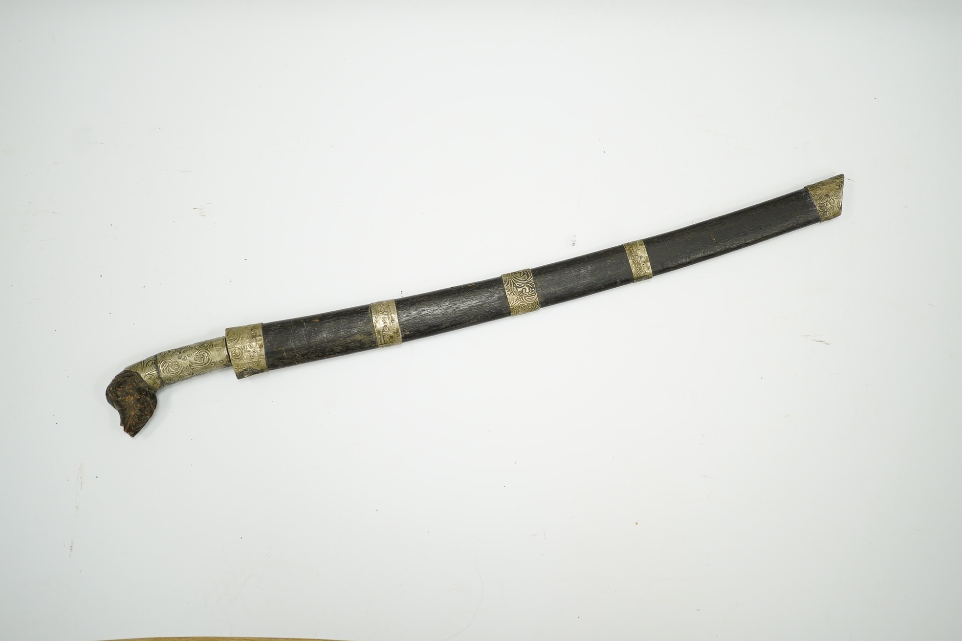 A Malaysian sword Parang, with broad curved pattern welded single edged blade, carved horn pommel, and embossed nickel mounts, in its wooden scabbard. Condition - good